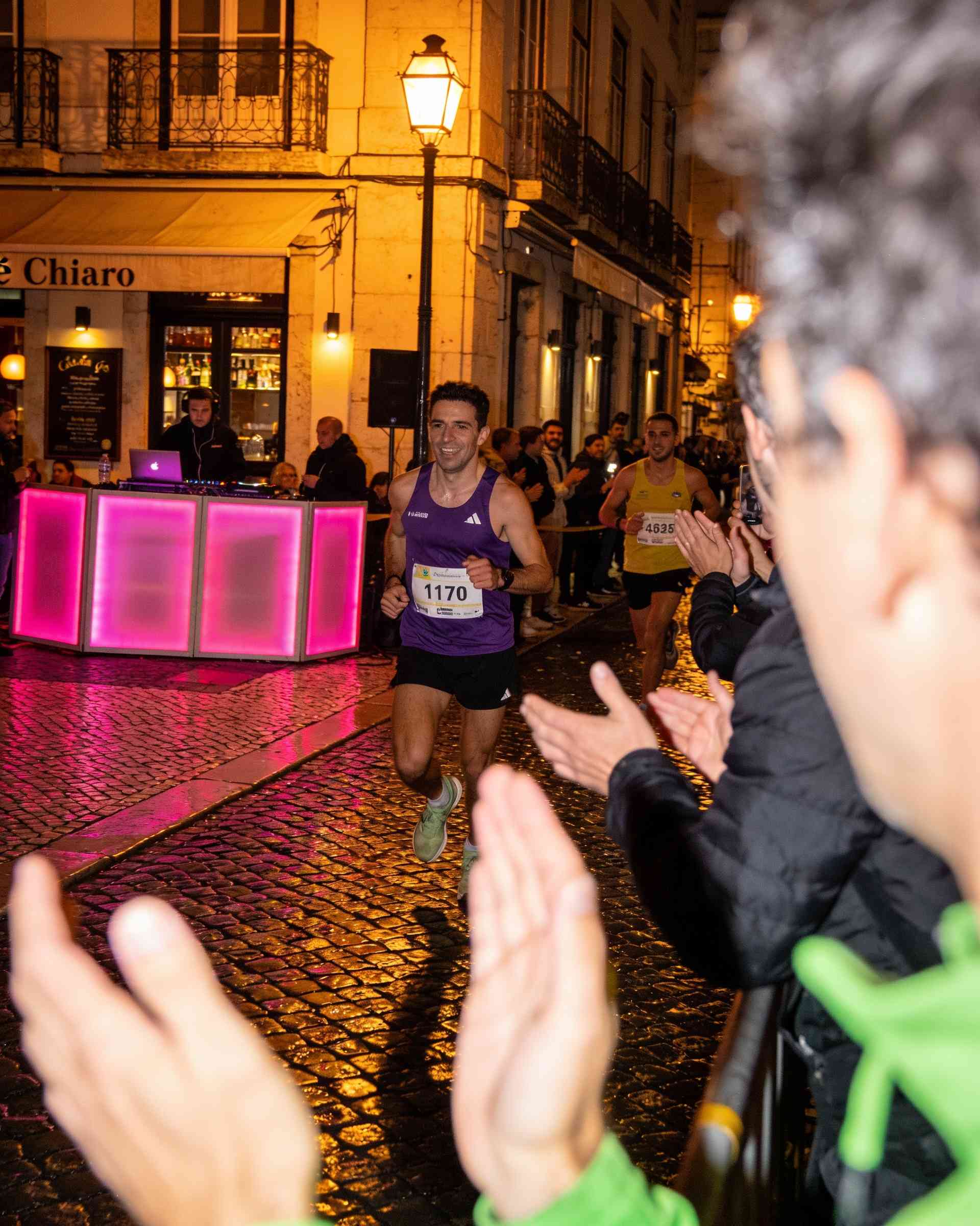 Chiado in Lisbon at night, lit in magenta and violet, runners passing