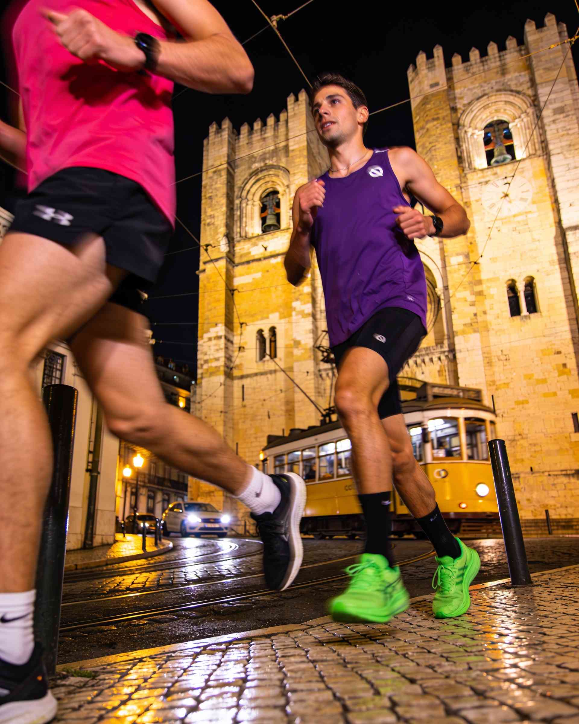 Lisbon Cathedral in Lisbon at night, lit in magenta and violet, runners passing