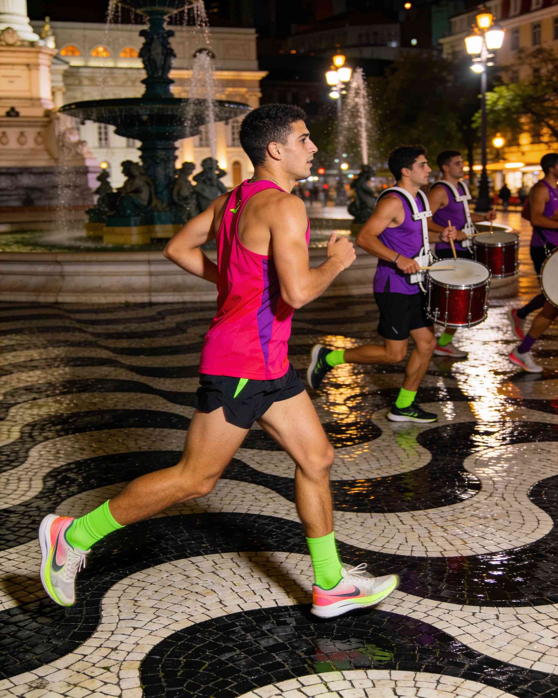 Rossio in Lisbon at night, lit in magenta and violet, runners passing