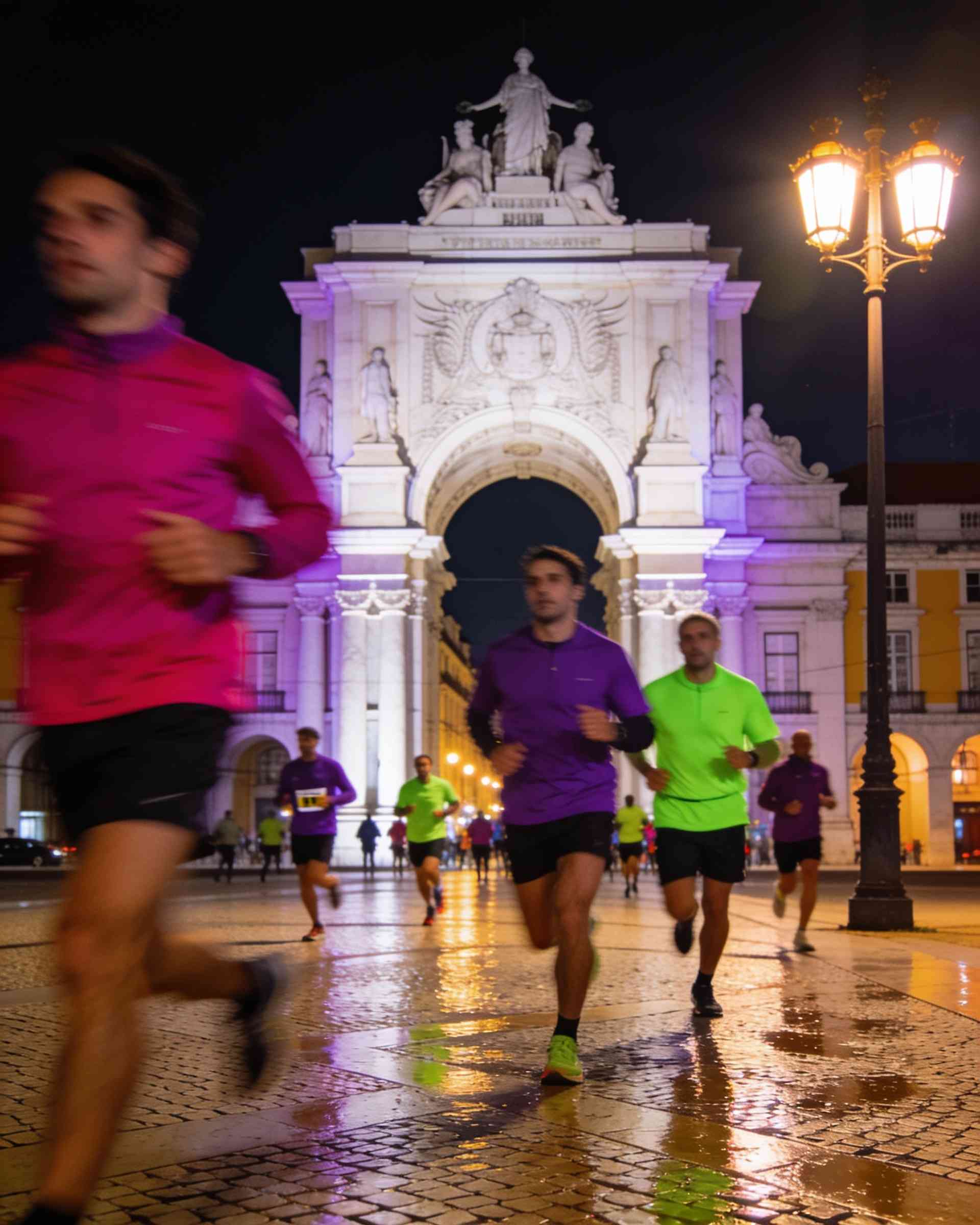 Rua Augusta Arch in Lisbon at night, lit in magenta and violet, runners passing